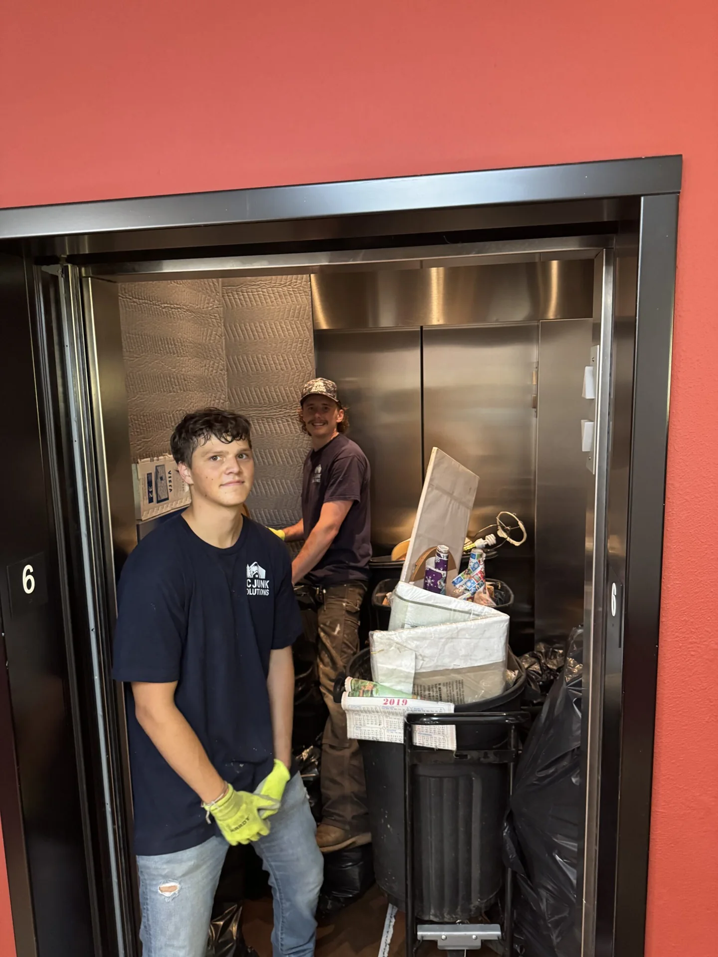 Two JC Junk Solutions crew members moving items through an elevator