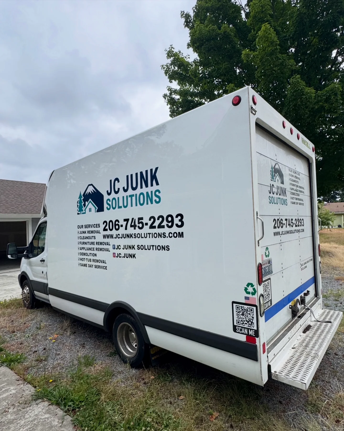 Rear and side of the JC Junk Solutions box truck at a residential property
